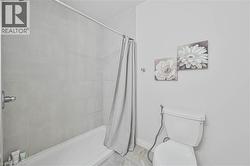 Bathroom featuring a white bathtub, light grey wall tiling, and a white toilet - 
