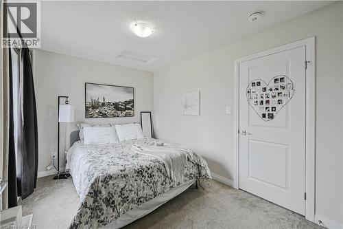 Carpeted room featuring a white paneled door, flush-mount ceiling light, and a window with dark curtains - 720 Grey Street Unit# 34, Brantford, ON - Indoor Photo Showing Bedroom
