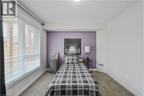Carpeted room featuring a large window with horizontal blinds, a single accent wall, and white trim - 720 Grey Street Unit# 34, Brantford, ON - Indoor Photo Showing Bedroom