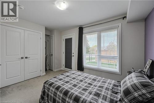 Bedroom featuring a large window with horizontal blinds, a white paneled door, a glass-paneled exterior door with internal blinds, and light gray wall-to-wall carpeting - 720 Grey Street Unit# 34, Brantford, ON - Indoor Photo Showing Bedroom