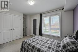 Bedroom featuring a large window with horizontal blinds, a white paneled door, a glass-paneled exterior door with internal blinds, and light gray wall-to-wall carpeting - 