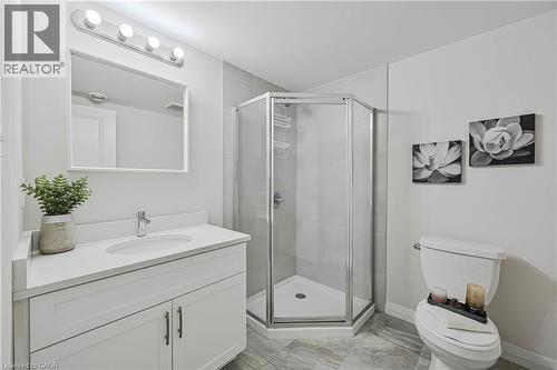 Modern bathroom featuring a white vanity with an integrated sink, a frameless rectangular mirror, and an enclosed corner shower with a glass door - 720 Grey Street Unit# 34, Brantford, ON - Indoor Photo Showing Bathroom