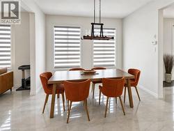 Dining area featuring light-toned tile flooring, three large windows with banded shades, and a linear chandelier with exposed bulbs - 