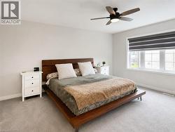 Bright bedroom featuring light gray carpeting, a large multi-pane window with a roller shade, and a dark wood ceiling fan - 