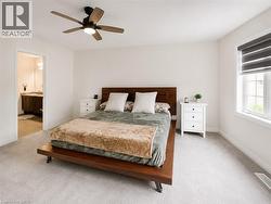 Carpeted bedroom with a ceiling fan, a window featuring privacy blinds, and an entryway to a bathroom - 