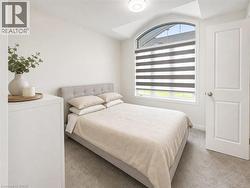 Bedroom featuring an arched window with integrated blinds, light gray carpeting, a paneled door, and a flush-mount ceiling light - 