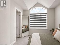 Bedroom featuring a large arched window with custom blinds, vaulted ceiling detail, and light-toned carpet flooring - 