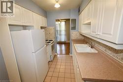 Galley kitchen featuring white cabinetry, a double basin sink, light-colored tile flooring, and white appliances including a refrigerator and electric range - 