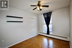 Light-filled room featuring parquet wood-finish flooring, a ceiling fan with integrated lighting, and a large window with a baseboard heating unit below - 