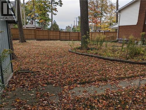 Spacious backyard featuring a wood fence, mature trees, concrete patio area, and defined planting beds - 462 Hazel Street, Waterloo, ON 