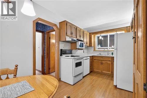 Kitchen featuring hardwood flooring, wood cabinetry, white appliances, solid surface countertops, and a double basin sink - 525 East 16Th Street, Hamilton, ON - Indoor Photo Showing Kitchen