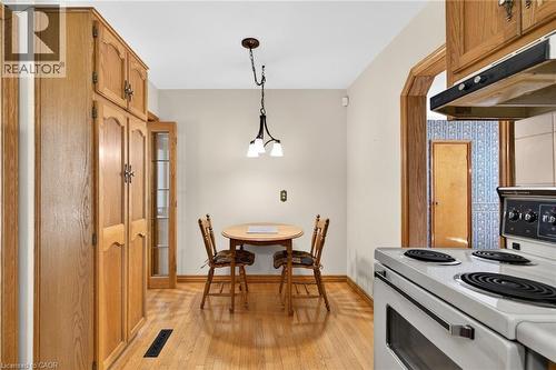 Bright eat-in kitchen area featuring wood-finish flooring, a three-light pendant fixture, and extensive built-in wood cabinetry - 525 East 16Th Street, Hamilton, ON - Indoor