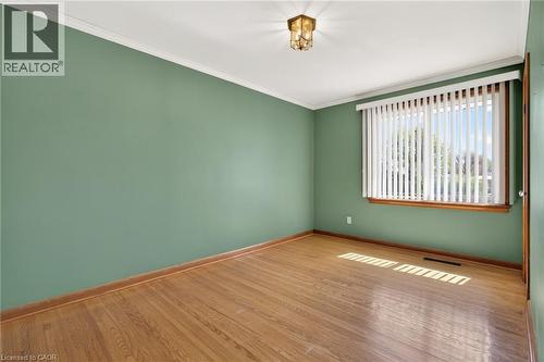 Room featuring wood-finish flooring, a large window with vertical blinds, and a flush-mount ceiling light fixture - 525 East 16Th Street, Hamilton, ON - Indoor Photo Showing Other Room