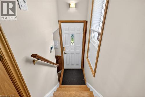 Entryway featuring a paneled door with decorative glass, wood-finish stair treads, a coordinating wood-finish handrail, light-toned wall paint, and a window with wood-finish trim and cellular blinds - 525 East 16Th Street, Hamilton, ON - Indoor Photo Showing Other Room