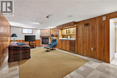 Recreational space featuring wood-paneled walls, a corner brick fireplace, and a built-in wet bar with cabinetry and a compact refrigerator - 525 East 16Th Street, Hamilton, ON - Indoor With Fireplace