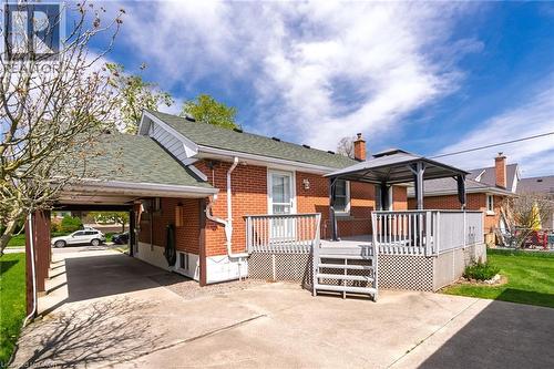 Red brick exterior featuring a covered carport, multi-level wooden deck with lattice skirting, and a spacious concrete patio - 525 East 16Th Street, Hamilton, ON - Outdoor With Deck Patio Veranda