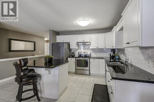 Contemporary kitchen featuring white cabinetry, dark countertops, stainless steel appliances, a subway tile backsplash, and light-toned floor tiles - 605 Welland Avenue Unit# 21, St. Catharines, ON - Indoor Photo Showing Kitchen With Double Sink