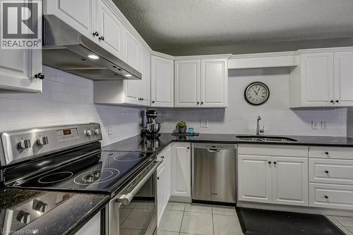 Kitchen featuring white cabinetry, dark countertops, tile flooring, a stainless steel range hood, and stainless steel appliances - 605 Welland Avenue Unit# 21, St. Catharines, ON - Indoor Photo Showing Kitchen With Double Sink