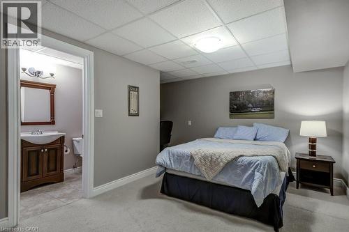 Carpeted room with drop ceiling and recessed lighting, offering direct access to a bathroom featuring a dark wood vanity with white sink, a framed mirror, and tile flooring - 605 Welland Avenue Unit# 21, St. Catharines, ON - Indoor Photo Showing Bedroom