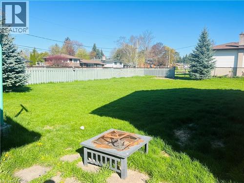 Expansive green lawn featuring a privacy fence, two mature evergreen trees, and a built-in fire pit - 157 Schweitzer Street, Kitchener, ON - Outdoor With Backyard