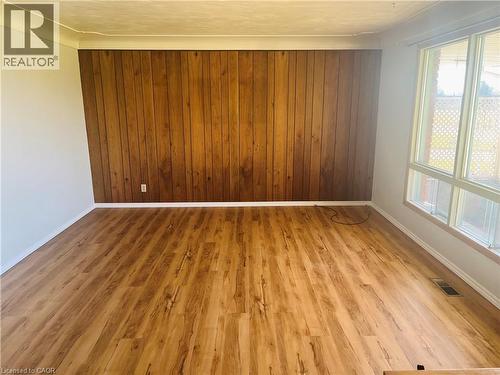 Spacious interior room featuring wood-finish flooring, a prominent wood-paneled accent wall, white painted walls, and large multi-pane windows providing abundant natural light - 157 Schweitzer Street, Kitchener, ON - Indoor Photo Showing Other Room