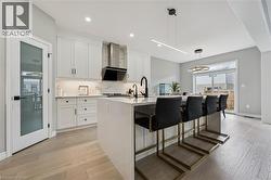 Contemporary kitchen featuring a waterfall island with seating, white shaker cabinetry, and wood-finish flooring - 