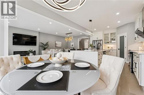 Open-concept living space featuring a contemporary dining area with a round glass-top table, light wood-finish flooring, a modern linear chandelier, and recessed lighting throughout - 628 Florencedale Crescent, Kitchener, ON 