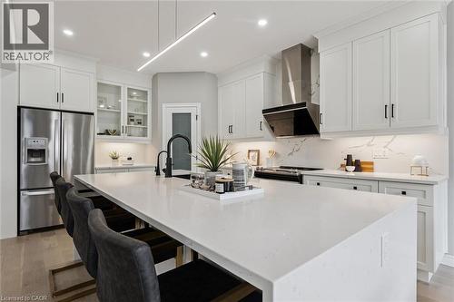 Modern kitchen featuring a large white island with seating, stainless steel appliances, white cabinetry with black hardware, and a matching white countertop and backsplash - 628 Florencedale Crescent, Kitchener, ON 