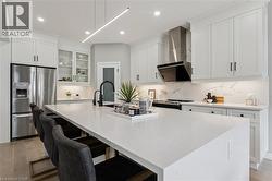 Modern kitchen featuring a large white island with seating, stainless steel appliances, white cabinetry with black hardware, and a matching white countertop and backsplash - 