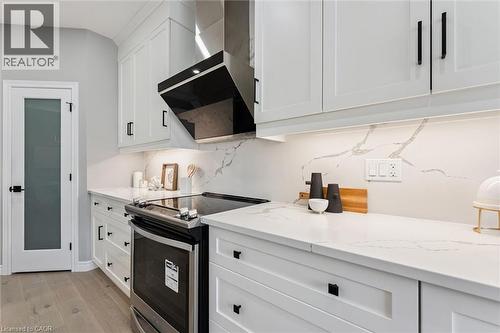 Contemporary kitchen featuring white shaker cabinetry, stainless steel range with overhead ventilation, light-toned countertops with integrated backsplash, and wood-finish flooring - 628 Florencedale Crescent, Kitchener, ON 