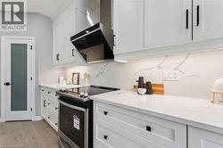 Contemporary kitchen featuring white shaker cabinetry, stainless steel range with overhead ventilation, light-toned countertops with integrated backsplash, and wood-finish flooring - 