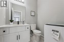 Bathroom featuring a white vanity with a light-toned countertop, a rectangular mirror, a chrome light fixture with three bulbs, a single-handle matte black faucet, and light gray wall paint - 