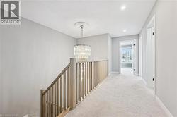 Upper-level hallway featuring a contemporary chandelier with ceiling medallion, light-toned wood banister, neutral carpeting, and recessed lighting - 