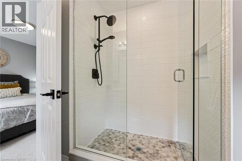Glass-enclosed shower with a matte black shower system, textured white subway tile, a recessed shower niche, and hexagonal floor tiling - 628 Florencedale Crescent, Kitchener, ON 
