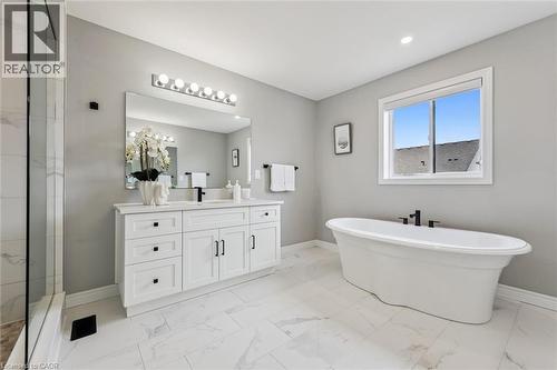 Spacious bathroom featuring a freestanding tub, a large vanity with dual sinks, a frameless glass shower enclosure, a wide window, and light-toned tile flooring - 628 Florencedale Crescent, Kitchener, ON 
