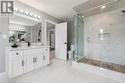Spacious bathroom featuring a frameless glass shower enclosure with white marble-look tile, a built-in shower niche, and a stone mosaic shower floor - 