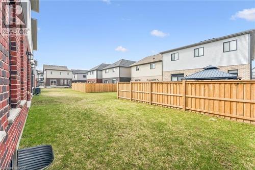 Expansive backyard featuring a manicured lawn, a full-height wood privacy fence, and a red brick exterior wall with a foundation window well - 628 Florencedale Crescent, Kitchener, ON 