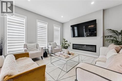 Living room featuring a built-in linear fireplace, wall-mounted television, recessed lighting, three vertical windows with modern blinds, and light-toned wall finishes - 628 Florencedale Crescent, Kitchener, ON 