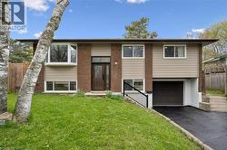 A bungalow featuring a brick and siding exterior, bay window, front entry with sidelight, integrated garage, and a sloped front lawn with mature trees - 