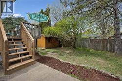 Expansive outdoor living area featuring a wood deck with stairs, a spacious lawn, a wooden privacy fence, a storage shed, and mature trees - 