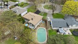 Oval-shaped in-ground pool with surrounding paved patio, situated beside a multi-level residential structure featuring a light brown shingle roof and a brick chimney - 