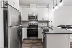 Kitchen featuring stainless steel appliances, a peninsula, dark countertops, dark wood-style flooring, and white cabinets - 