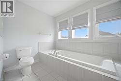 Bathroom featuring a built-in tub with chrome fixtures, three windows with privacy shades, and white tile surround - 