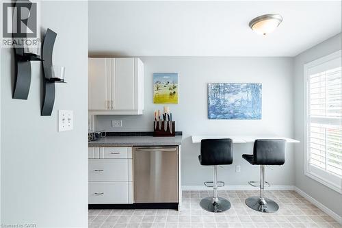 Kitchen area featuring white cabinetry, a stainless steel dishwasher, and a dark countertop - 560 Penny Lane, Waterloo, ON 