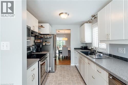 Galley kitchen featuring white cabinetry, gray speckled countertops, stainless steel appliances, a black sink, and a tiled backsplash - 560 Penny Lane, Waterloo, ON 