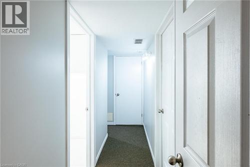 Hallway featuring light gray walls, dark carpet flooring, and white paneled doors with brushed nickel hardware - 560 Penny Lane, Waterloo, ON 