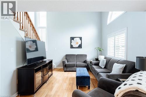 Living area featuring vaulted ceilings, wood-finish flooring, a prominent staircase with wood banisters, and a large window with plantation shutters - 560 Penny Lane, Waterloo, ON 