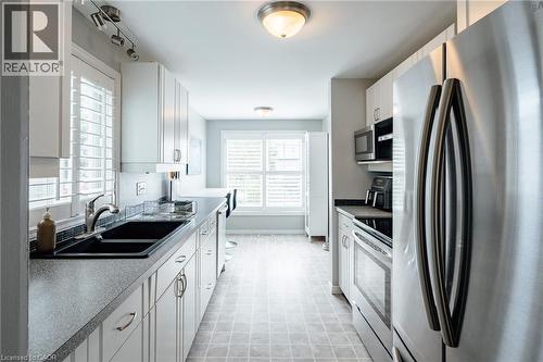 Galley kitchen featuring white cabinetry, stainless steel appliances, a double basin sink, and shuttered windows - 560 Penny Lane, Waterloo, ON 