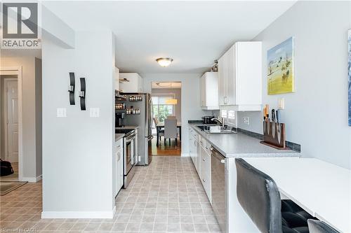 Galley kitchen featuring white cabinetry, stainless steel appliances, and an integrated breakfast bar - 560 Penny Lane, Waterloo, ON 