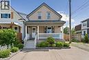 Two-story property featuring a front porch with white railing, a dormer window, and a dark metal roof - 180 Campbell Avenue, Hamilton, ON 
